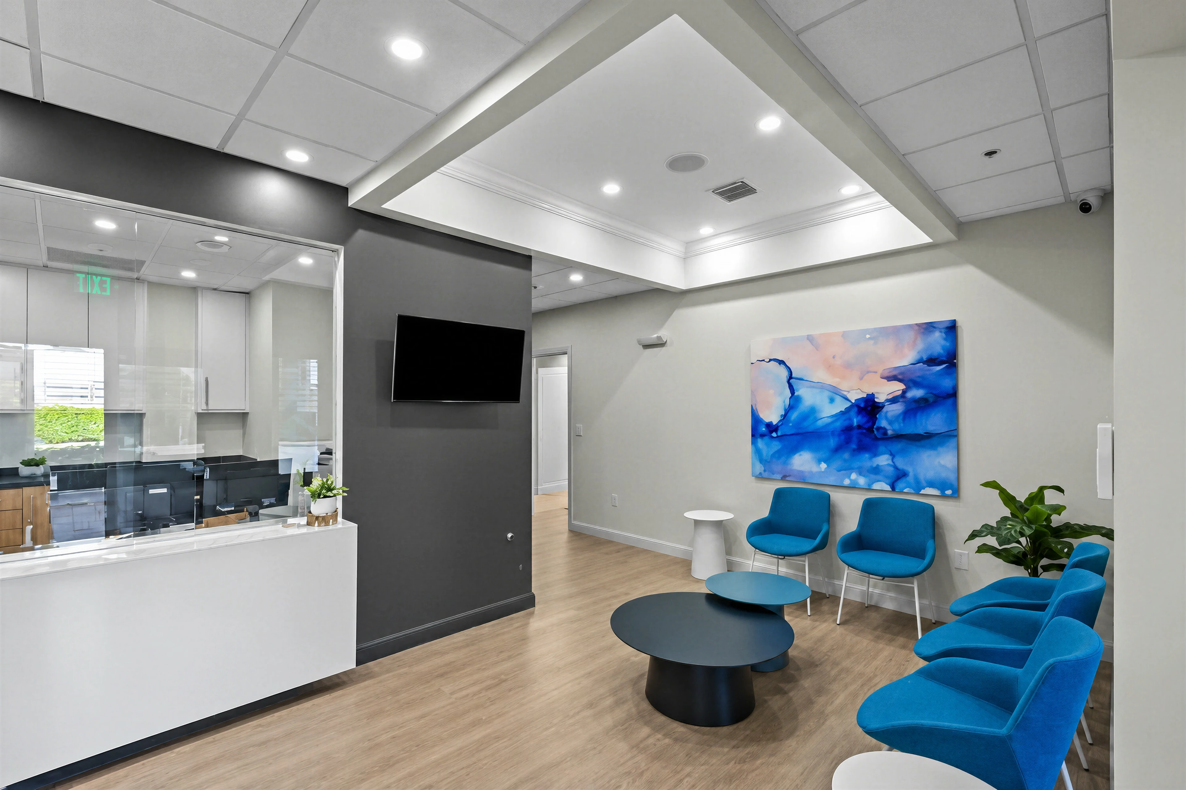 Reception and waiting area with blue chairs, wood-look flooring and glass partitions.